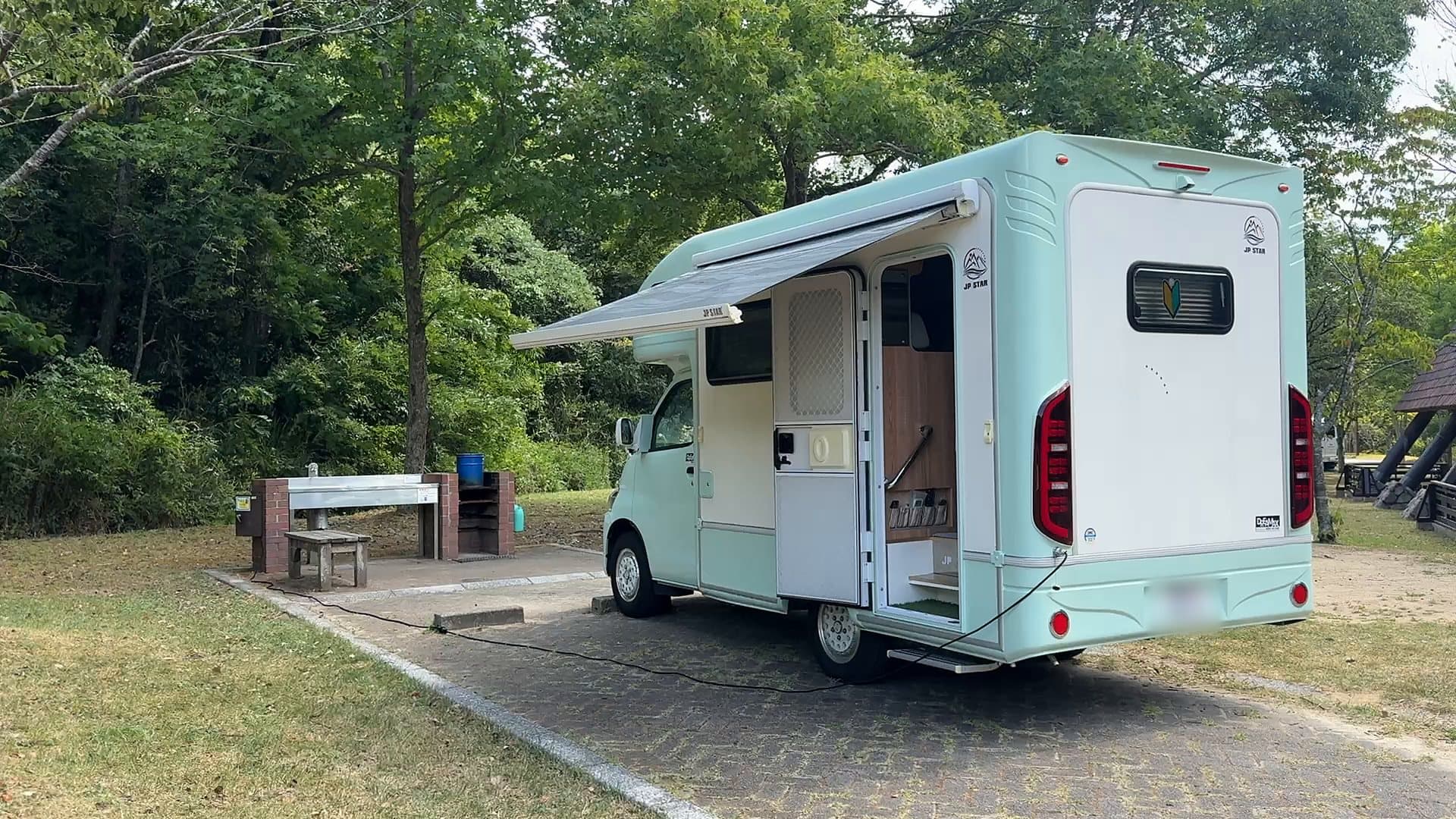 ドアを開け、オーニングを広げて公園のキャンプ場に停まる Treasure 1